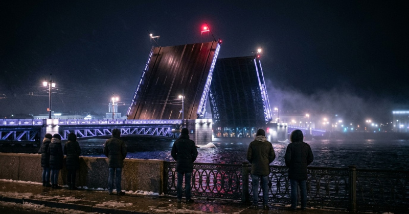 Ночь в Петербурге, мокрый снег: люди на гранитной набережной смотрят на разведённый мост, на вершине поднятого пролёта горит один красный огонь